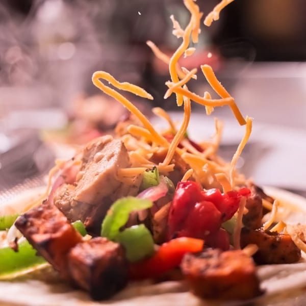 Steaming hot fajitas with chicken, colorful peppers, and shredded cheese falling onto the dish.