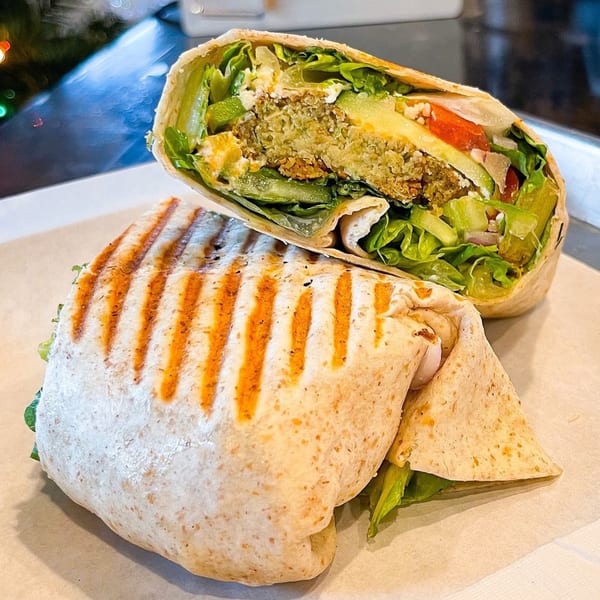 A grilled falafel wrap, cut in half, revealing fresh lettuce, tomatoes, and avocado.