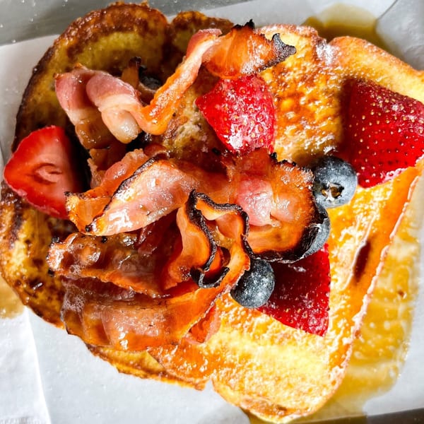 Golden French toast topped with crispy bacon, fresh strawberries, blueberries, and powdered sugar.
