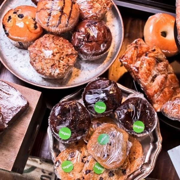 Assortment of BarleyBean muffins, cookies, and pastries, some labeled "Vegan," wrapped in plastic.