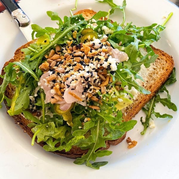BarleyBean's avocado toast with arugula, seeds, feta, and pickled onions on a white plate.