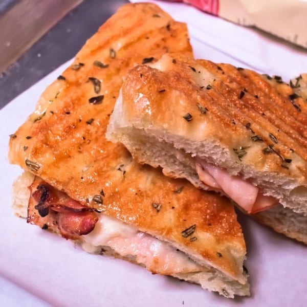 Two halves of a grilled panini sandwich with ham and melted cheese on a white plate.