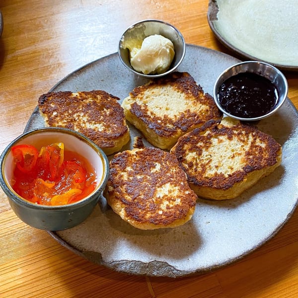 Four pieces of golden-brown French toast with sides of butter, blueberry jam, and fruit preserves.