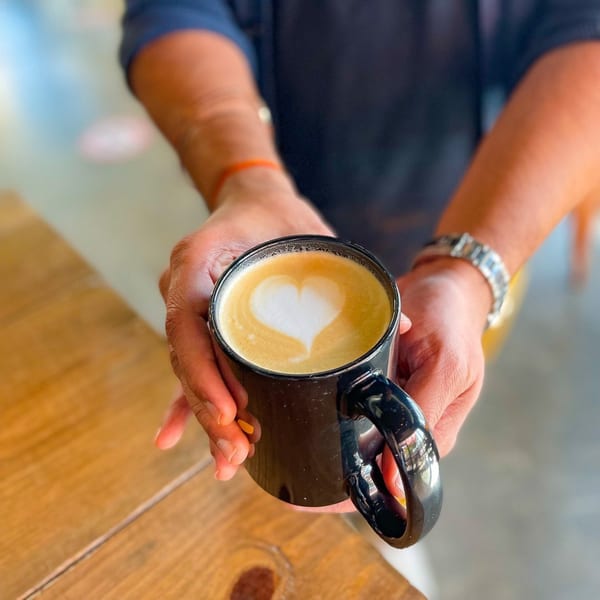 Hands holding a black mug of latte with a heart design in the foam at BarleyBean cafe.